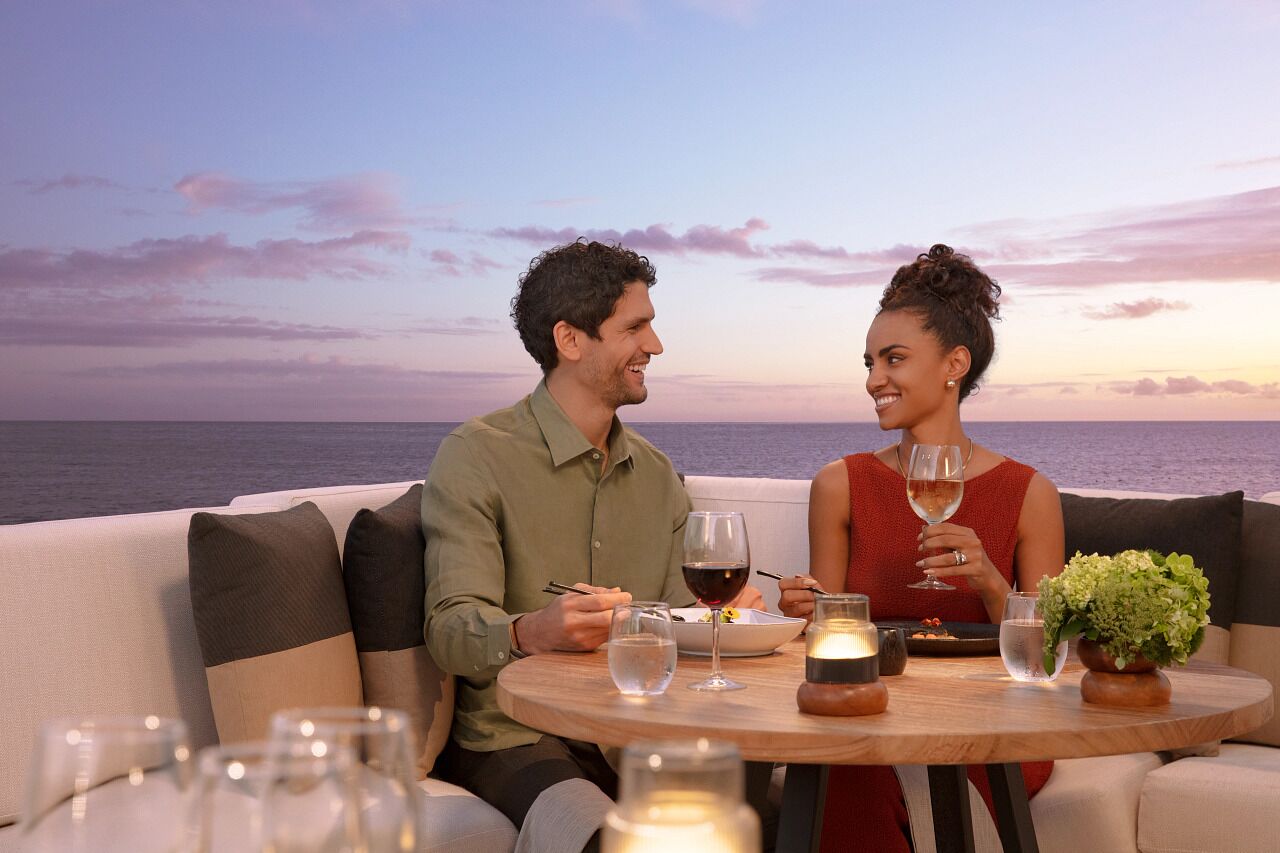 Un couple est assis à une table, devant laquelle s’étend une vue sur l’océan.