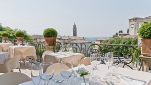 A terrace with tables set for dining, overlooking a cityscape with a prominent tower and buildings. - Albergo Al Sole (Asolo)