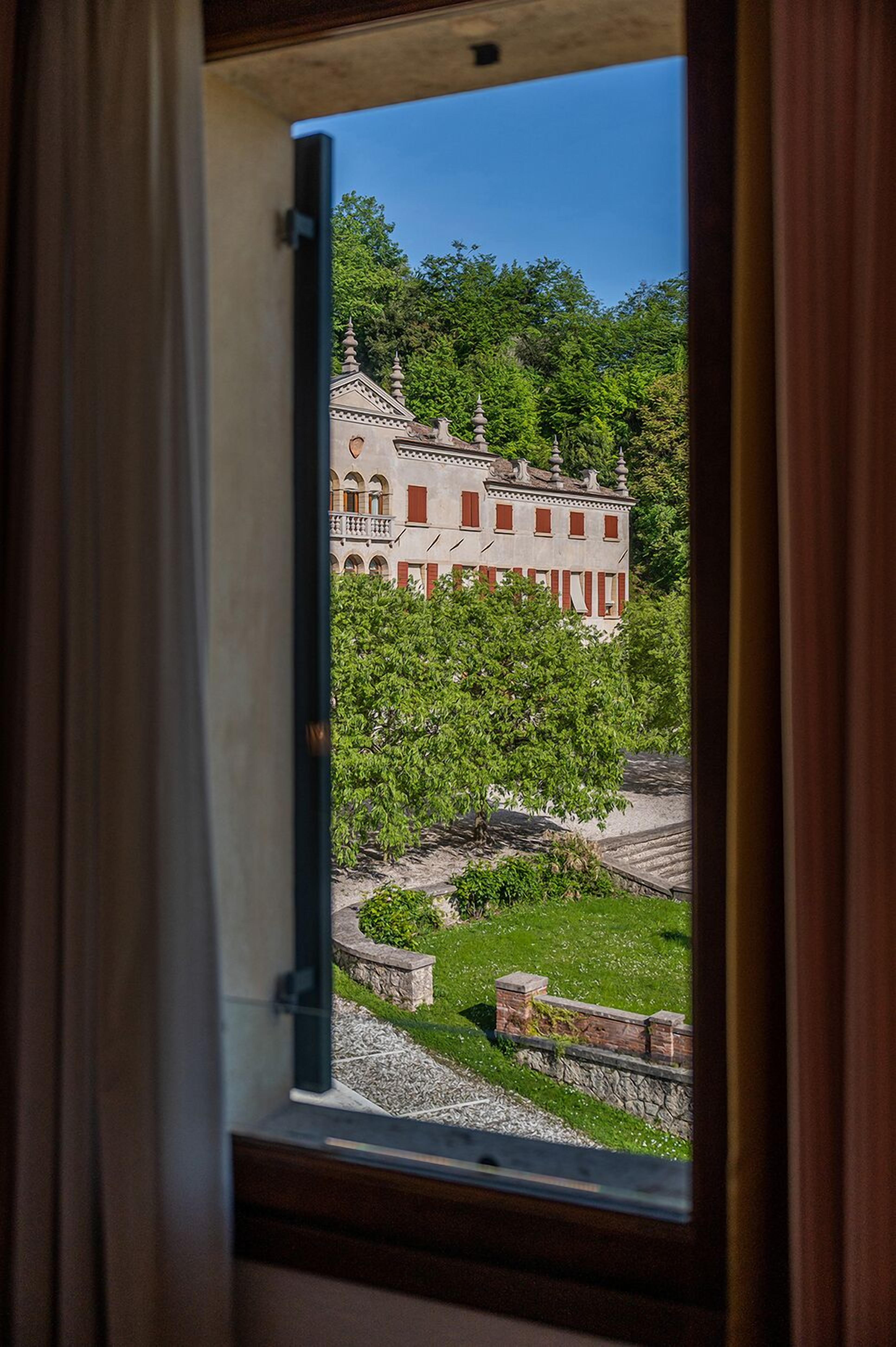 A view through a window of a building with a garden and a large structure in the background.
