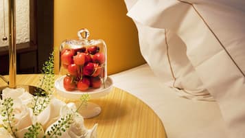 A neatly made bed with white linens, a bedside lamp, a glass jar with cherries, and a bouquet of white roses on a wooden bedside table.