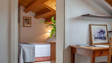 Una camera da letto con soffitto in legno, una scrivania con sedia, un comodino e un letto con coperta.