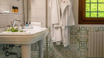 Une salle de bain équipée d’un lavabo, d’un miroir, d’un porte-serviettes et d’une fenêtre donnant sur un paysage verdoyant.