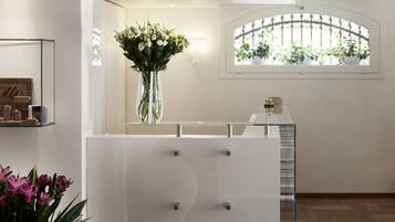 A reception area with a glass display case, a vase of flowers, and a window with potted plants.