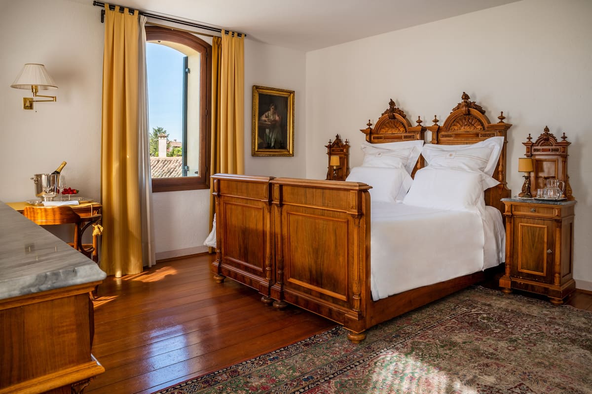 Un dormitorio con una cama grande de madera, una mesita de noche, un escritorio y una ventana con cortinas.