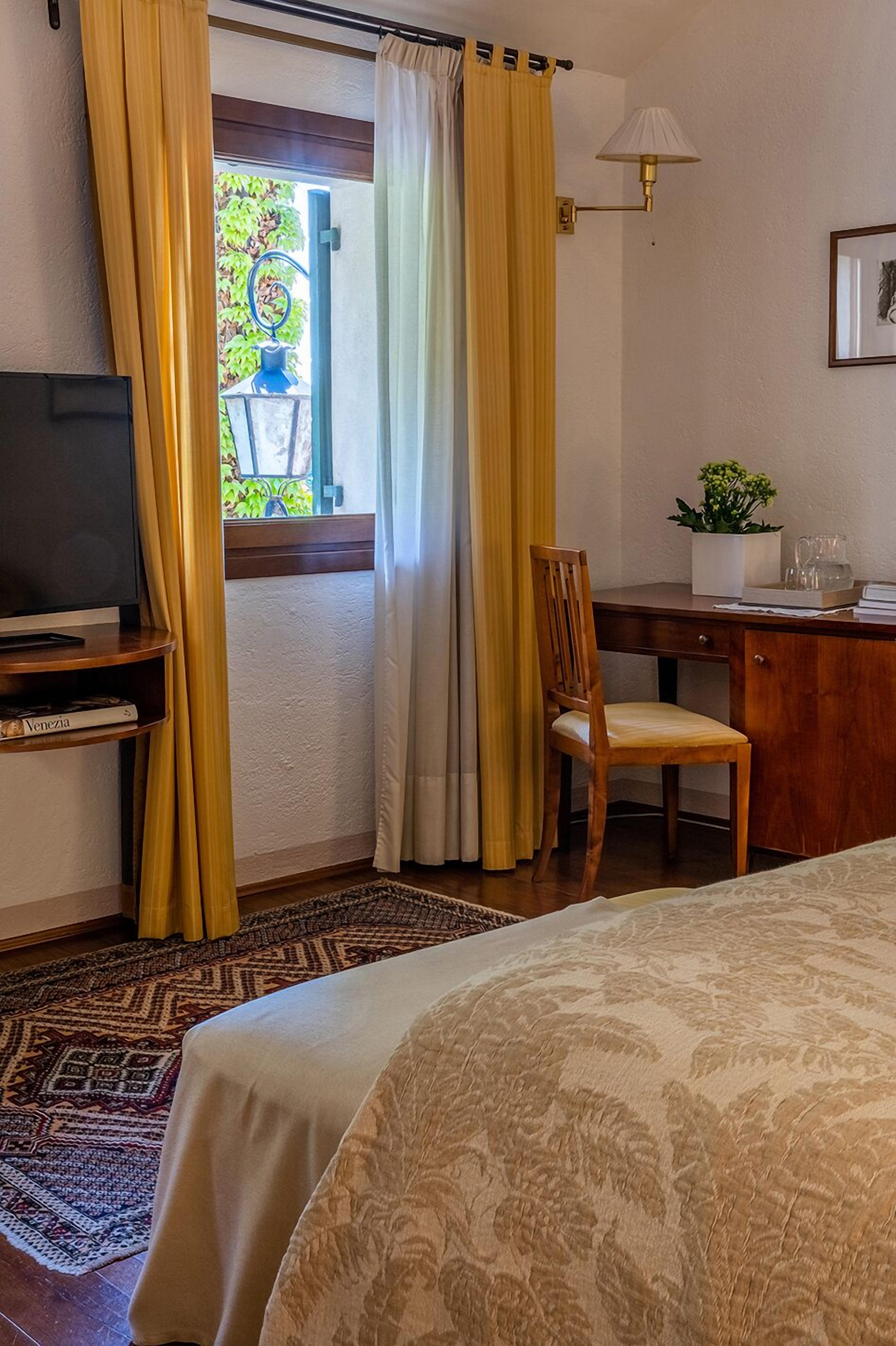 A hotel room with a bed, a desk with a chair, a television, a lamp, and a window with curtains.