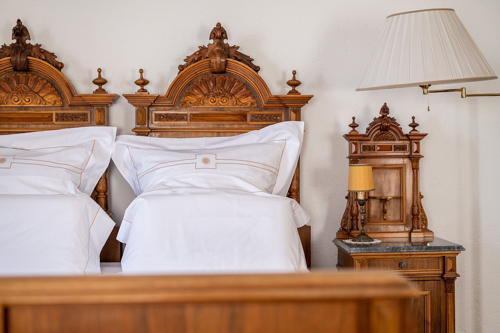A neatly made bed with white linens and a wooden headboard with intricate carvings.