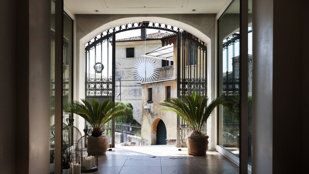 A corridor with a wrought iron gate, potted plants, and a view of a building with a balcony. - Albergo Al Sole (Asolo)