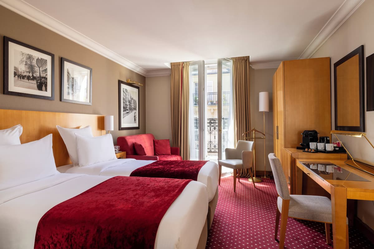 A hotel room with two beds, a desk with a chair, a coffee maker, and framed pictures on the wall.