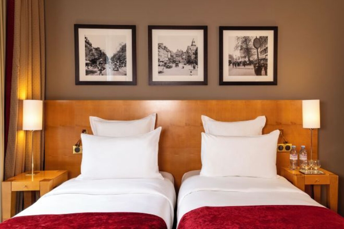 A hotel room with two beds, a wooden headboard, and three framed pictures on the wall.