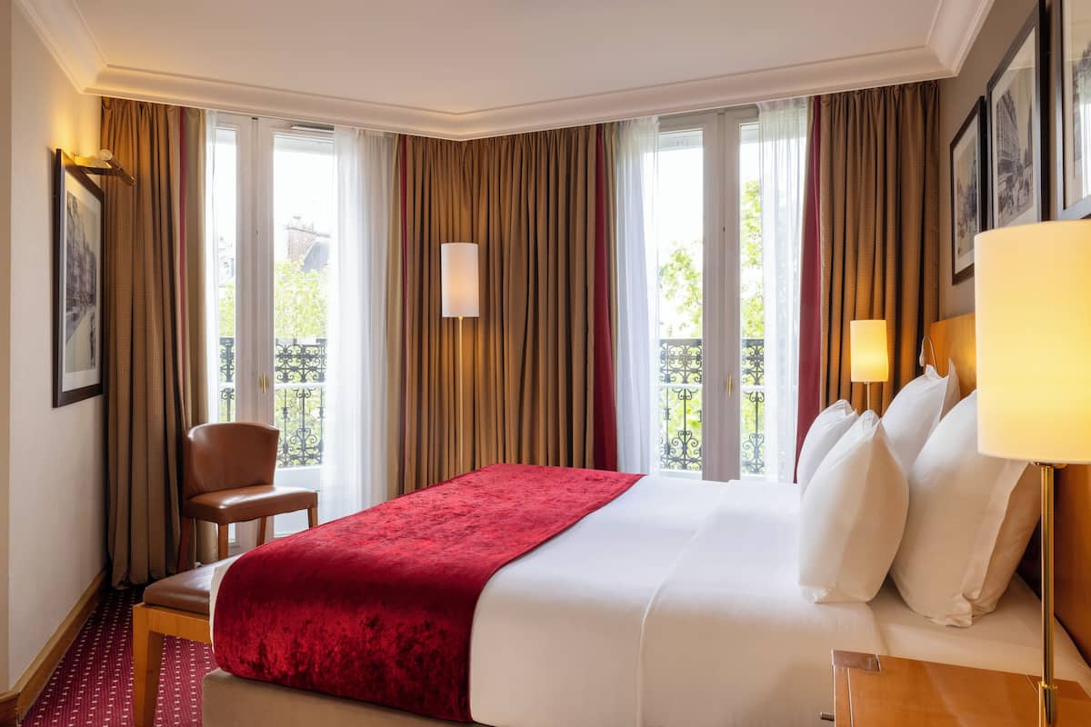 A hotel room with a large bed, a chair, a desk, and a window with curtains.