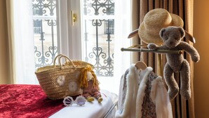 Una cama con un edredón rojo, una cesta de mimbre con un girasol, un osito de peluche y un sombrero de paja en un perchero.