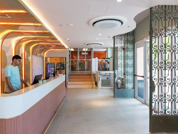 Zona de recepción de un hotel con un mostrador curvo, una escalera y una reja decorativa de hierro.