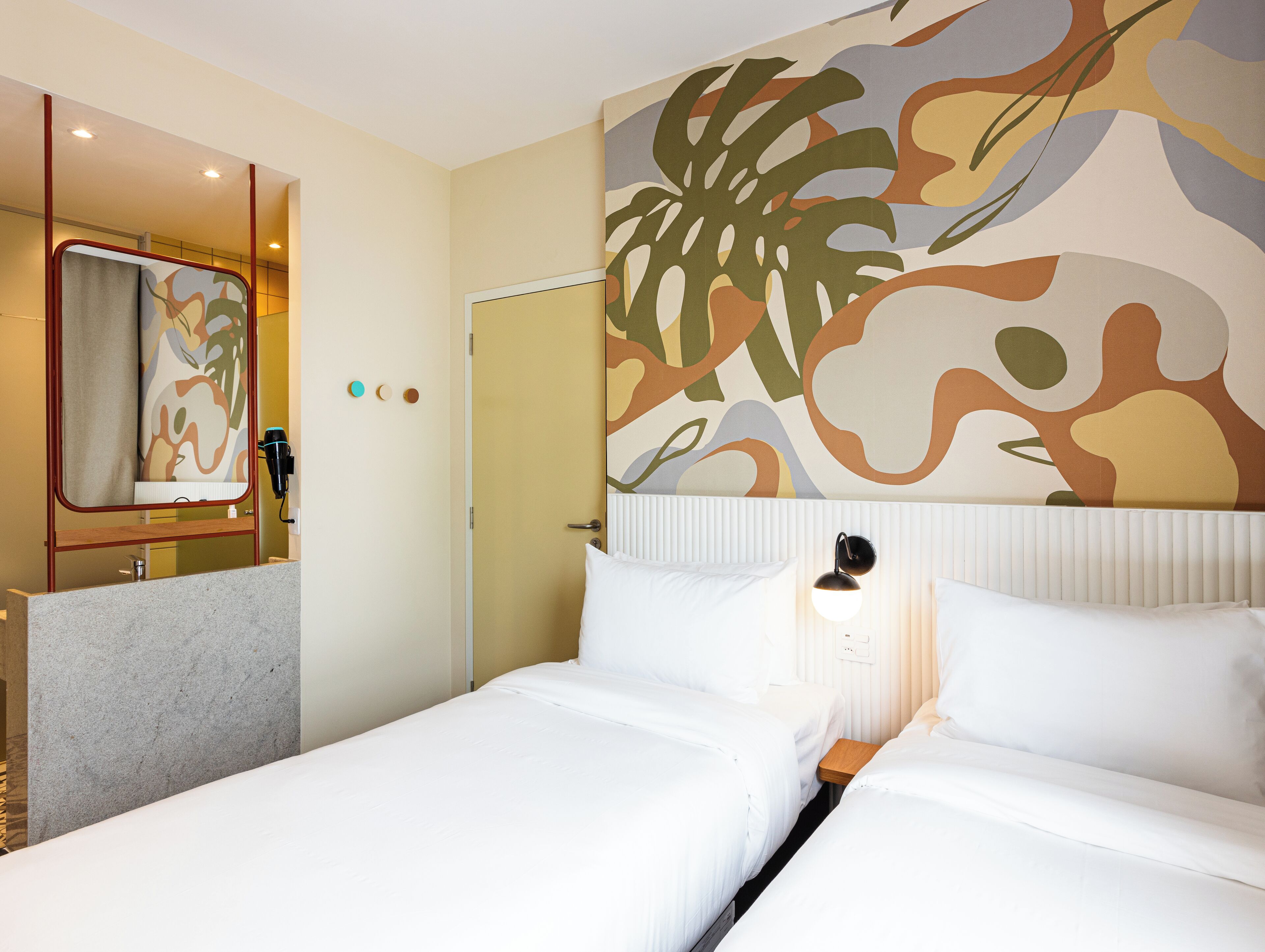 A hotel room with a bed, a nightstand, a mirror, and a wall with abstract art.