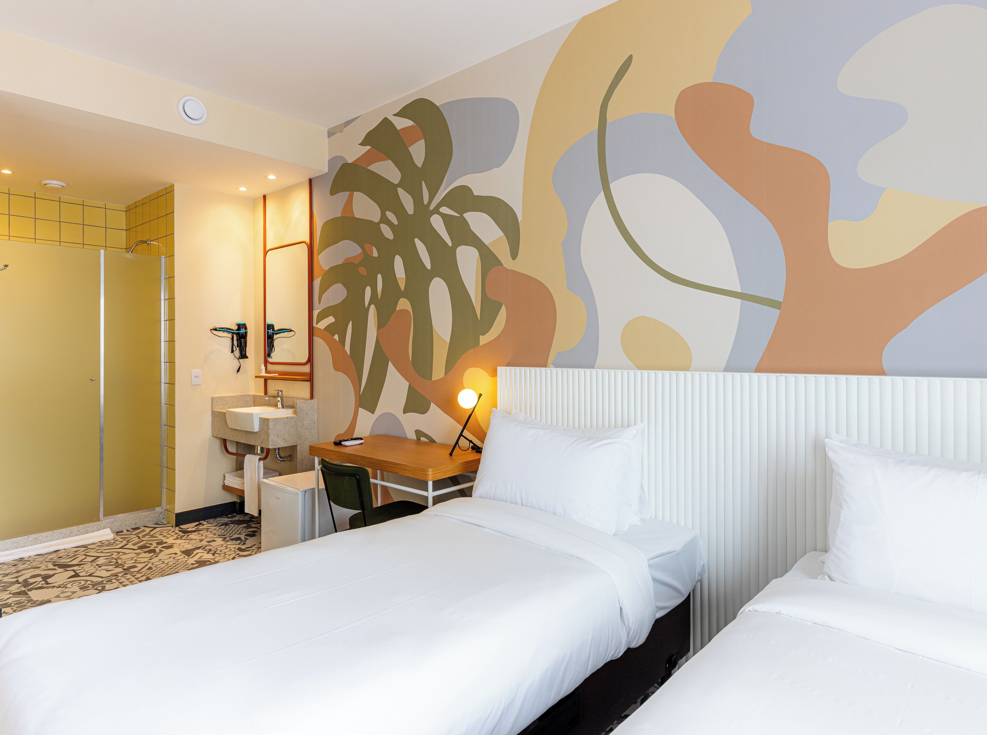 Habitación de hotel con dos camas, un escritorio, una silla, un lavamanos y un espejo.