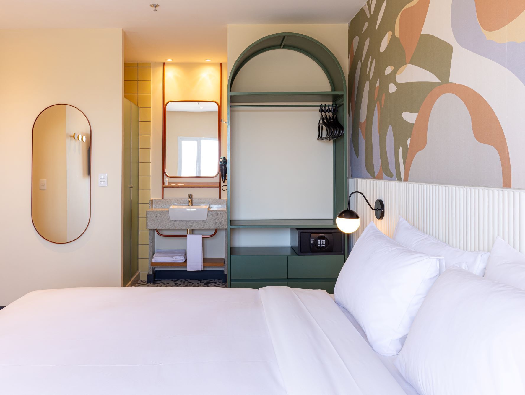 Habitación de hotel con una cama grande, un baño con lavamanos y espejo, y un teléfono en la pared.