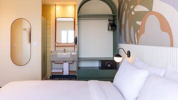Habitación de hotel con una cama grande, un baño con lavamanos y espejo, y un teléfono en la pared.