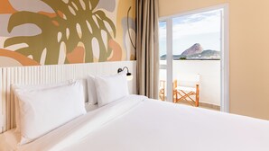 Habitación de hotel con una cama, vista a la montaña y al agua, y un balcón con sillas.
