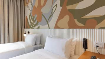 A hotel room with two beds, a wooden nightstand, a telephone, and a wall with abstract floral wallpaper.