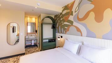 A hotel room with a large bed, a bathroom with a mirror and sink, and a wall with abstract art.