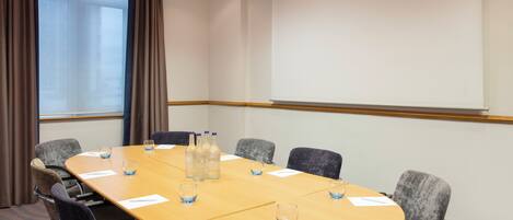 A conference room with a long table, six chairs, and a projector screen.