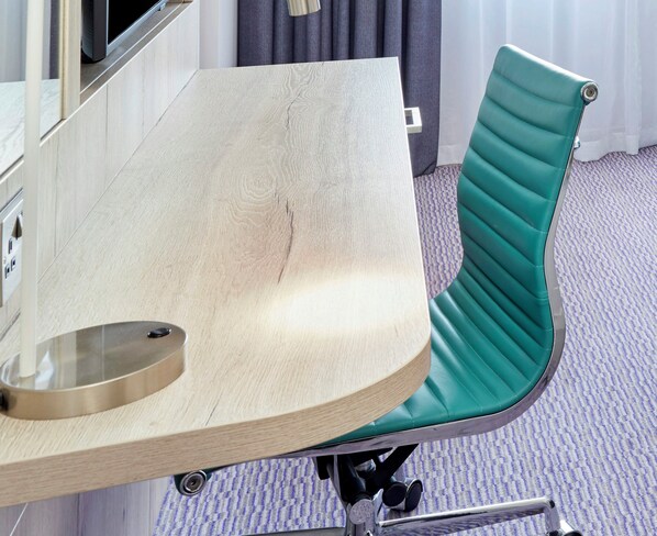 Une chambre d’hôtel moderne avec un bureau en bois et un fauteuil recouvert d’un tissu vert.