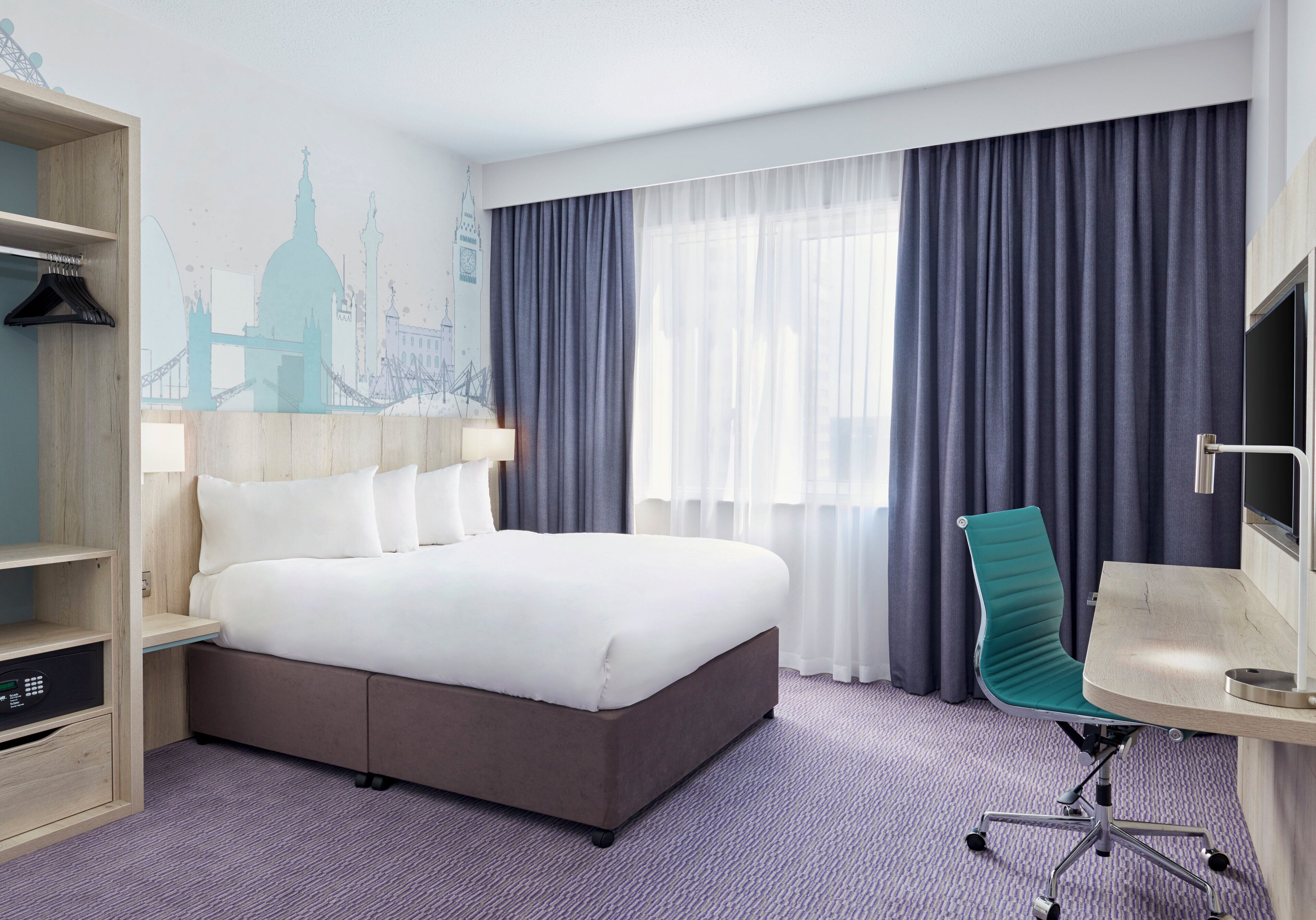 Een hotelkamer met een groot bed, een bureau, een stoel, een kledingkast en een muurschildering van een stadsgezicht.