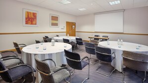 A conference room with multiple round tables, chairs, and a projector screen. - Leonardo Hotel London Croydon (Croydon)