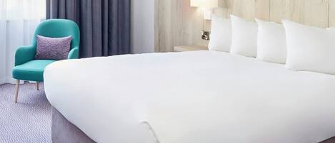 Une chambre d’hôtel avec un grand lit, une chaise, une lampe et un mur orné d’un motif décoratif.