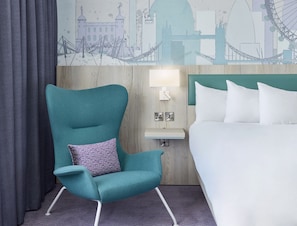 A teal armchair with a patterned pillow, a bedside table with a lamp, and a bed with white linens. - Leonardo Hotel London Croydon (Croydon)