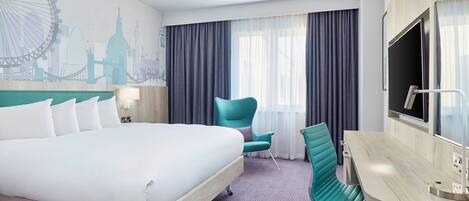 Habitación de hotel con una cama grande, un escritorio con una silla, un televisor y un mural con el horizonte de una ciudad.