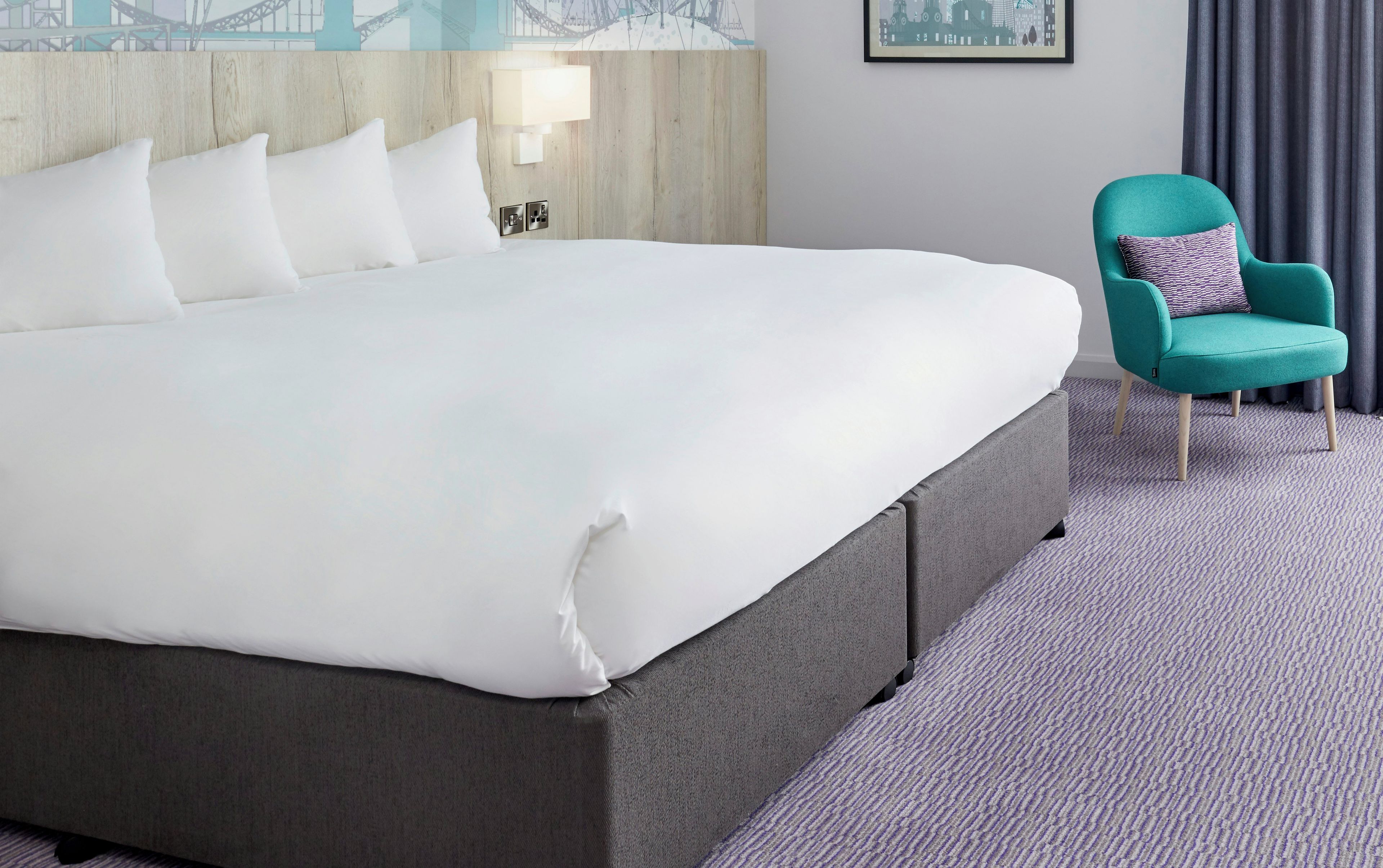 Et hotelværelse med en stor seng, en turkis lænestol og udsigt over bybilledet.