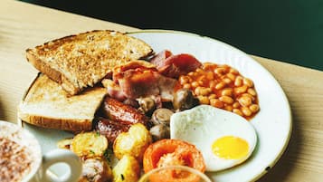 Prato de café da manhã com torradas, ovos, linguiça, feijão e um copo de suco de laranja.