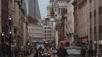 A busy city street with historic buildings, a prominent dome, and modern skyscrapers in the background.
