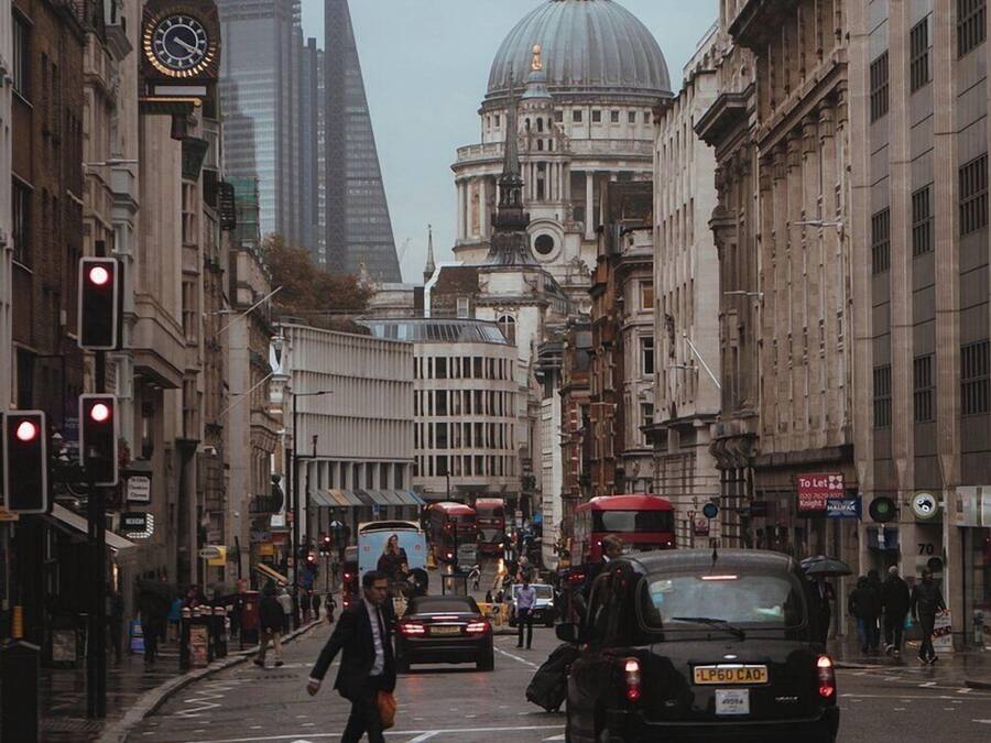 A busy city street with historic buildings, a prominent dome, and modern skyscrapers in the background.