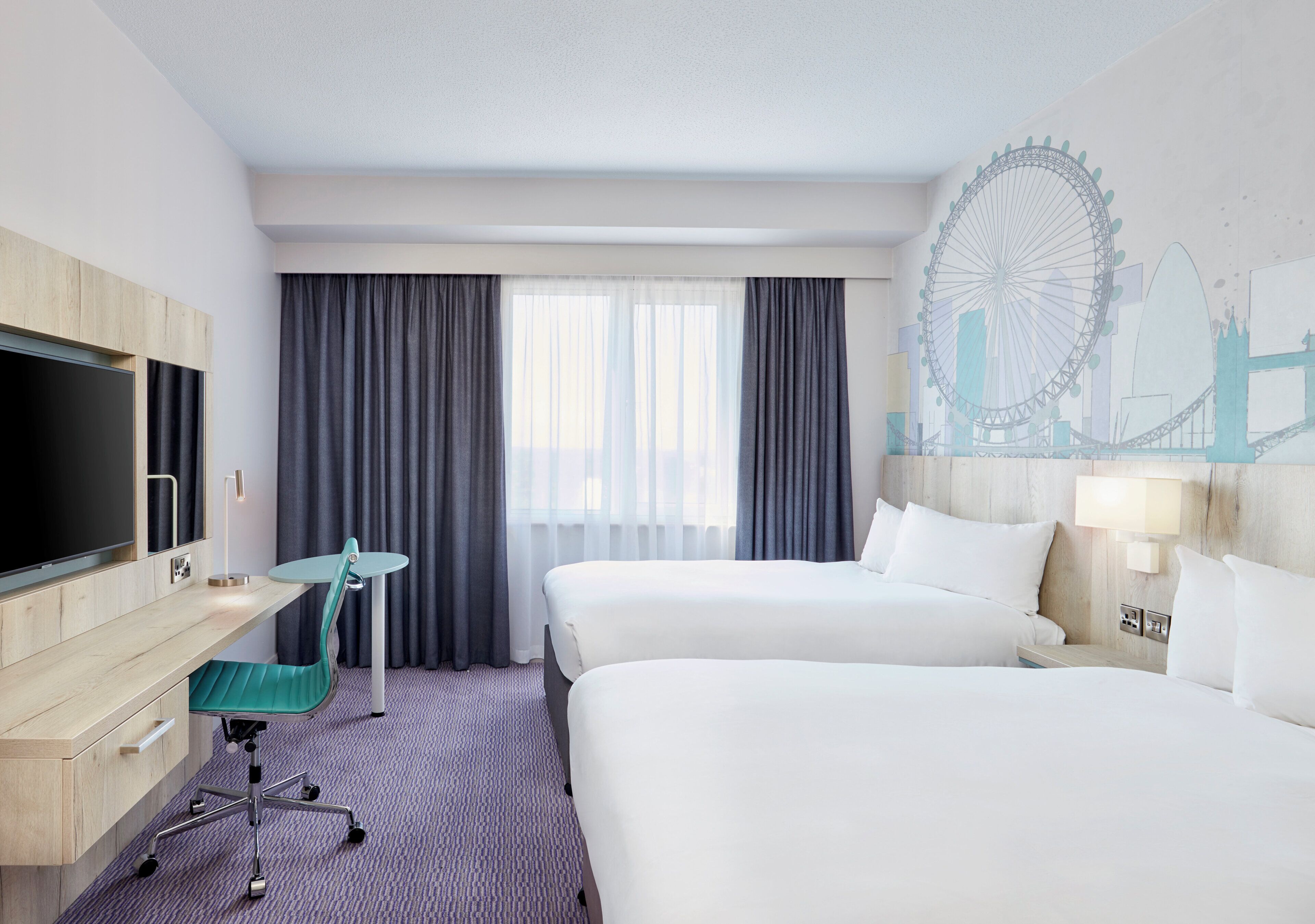 Hotelkamer met twee bedden, een bureau met stoel, een televisie en een muurschildering van een reuzenrad.