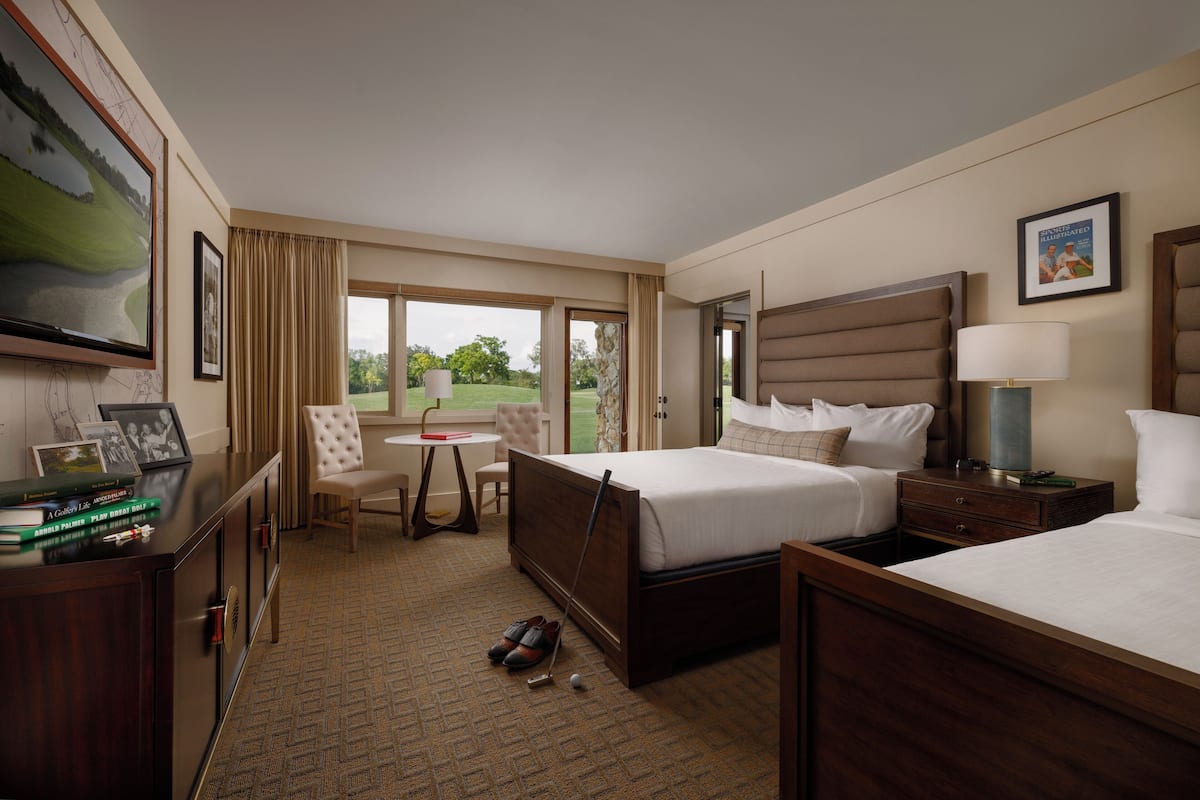 A hotel room with a bed, bedside table, lamp, and a view of the outdoors.