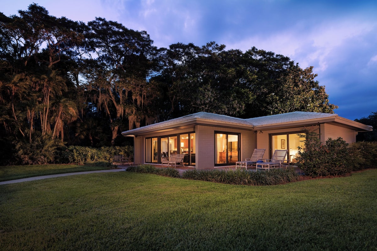 A modern house with a glass facade, a covered patio, and a well-maintained lawn.