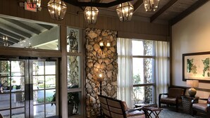 A lobby with a stone wall, wooden flooring, and a seating area with chairs and a table. - Arnold Palmer's Bay Hill Club & Lodge (Orlando)