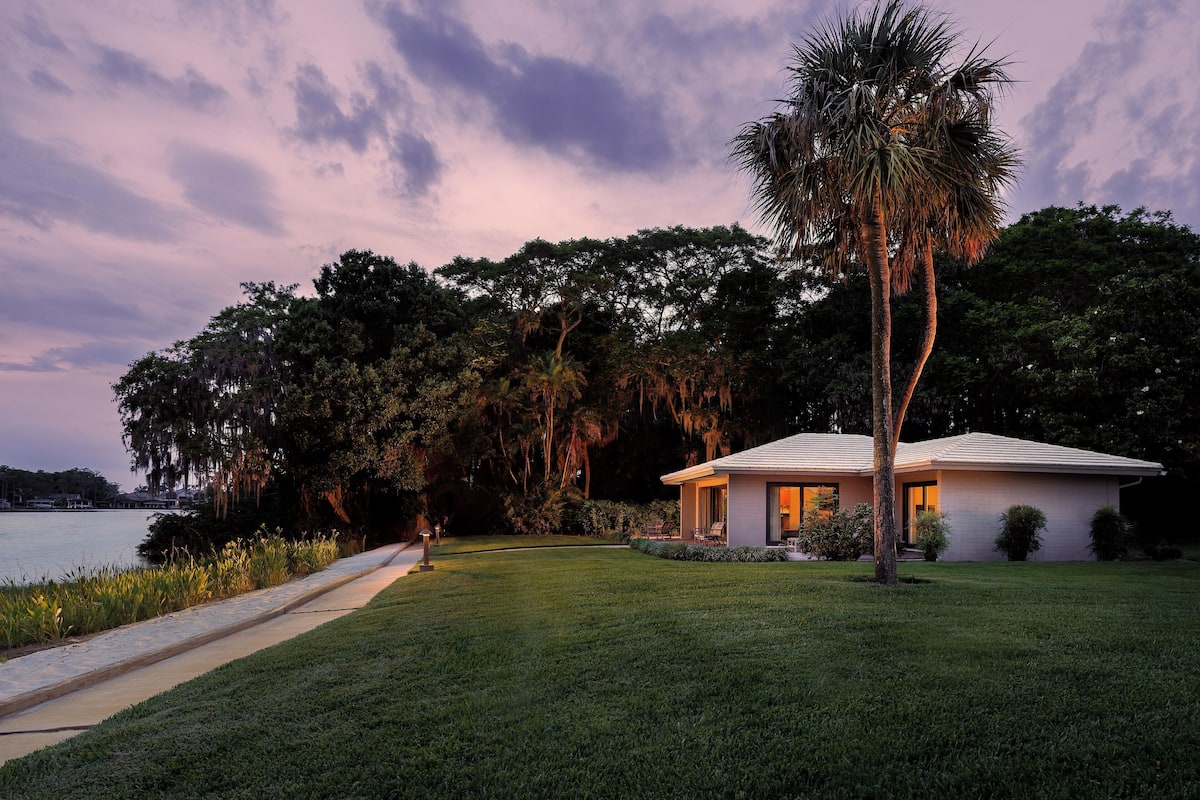 A house with a lawn, a pathway, and a body of water in the background.