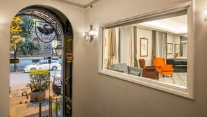 A hotel entrance with a grand archway, a large mirror reflecting the interior, and a potted plant on the floor.