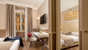 A hotel room with a bed, a desk with a chair, a television, and a window with curtains.