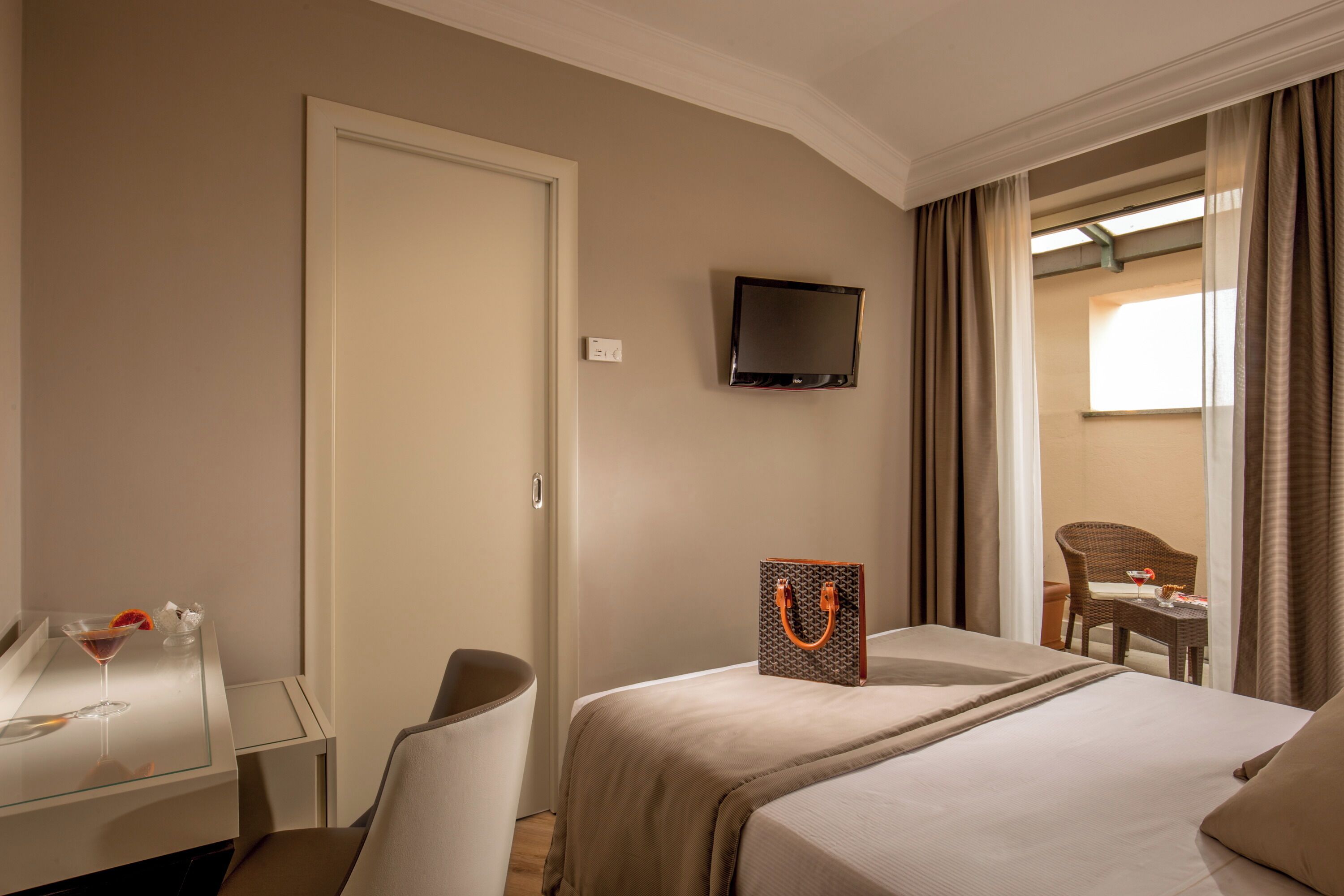 A hotel room with a bed, a desk with a chair, a television, and a view of an outdoor seating area.
