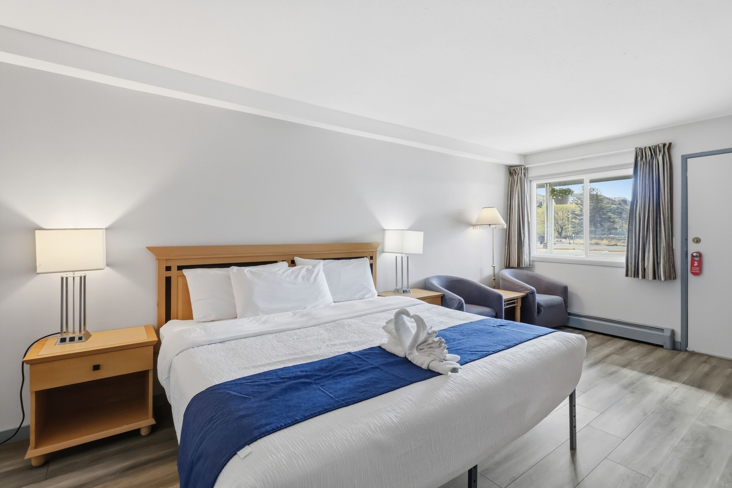 A hotel room with a bed, two bedside tables, a chair, a desk, and a window with curtains.