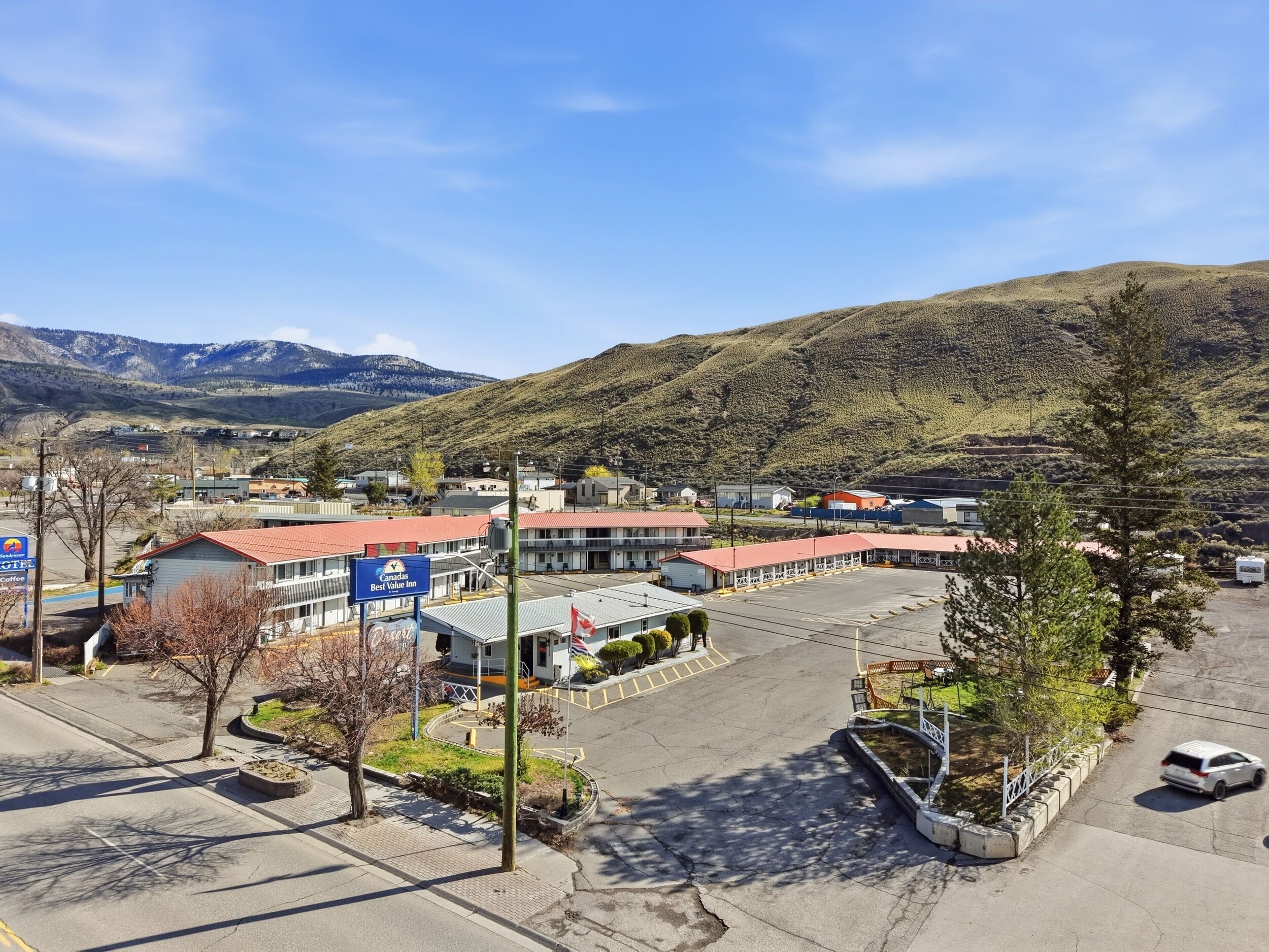 A hotel with a red roof, a parking lot, and a mountainous backdrop.