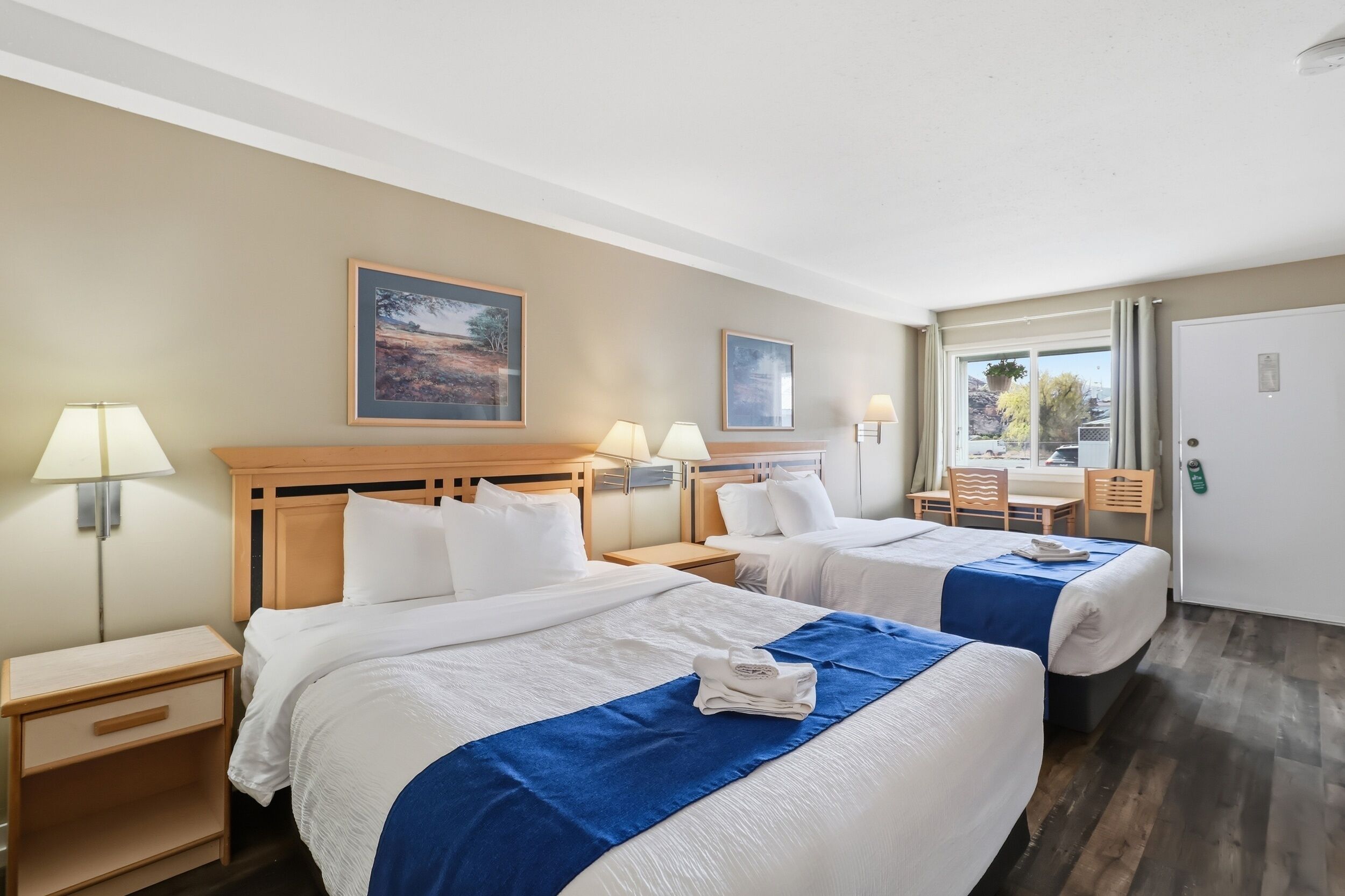 Habitación de hotel con dos camas, un escritorio, sillas y ventana con vistas.