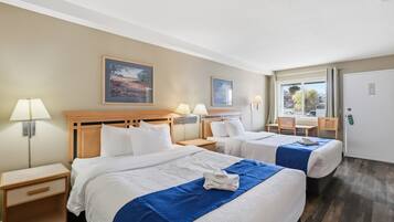 Habitación de hotel con dos camas, un escritorio, sillas y ventana con vistas.