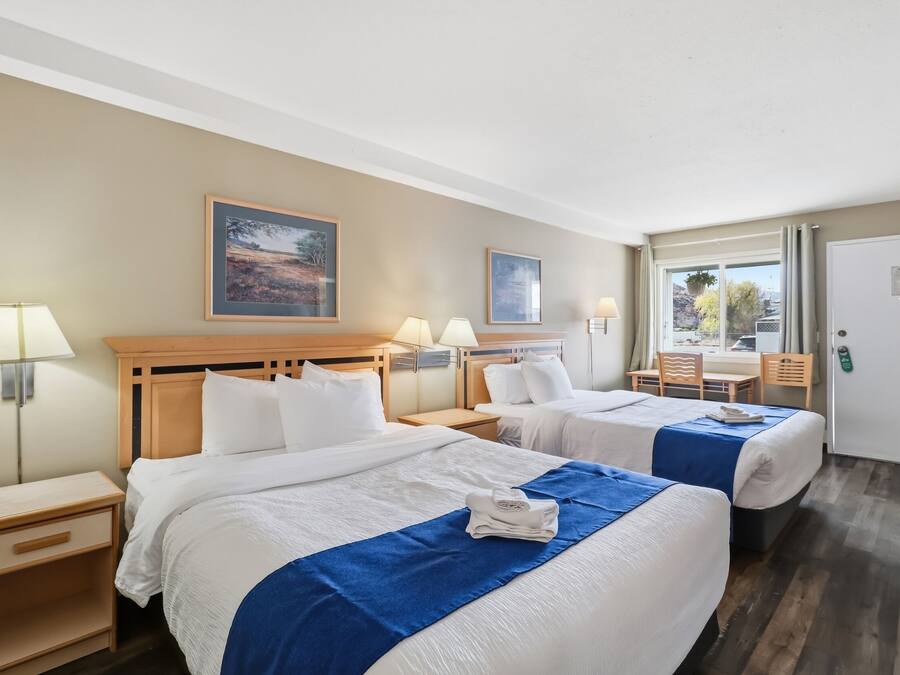 Habitación de hotel con dos camas, un escritorio, sillas y ventana con vistas.
