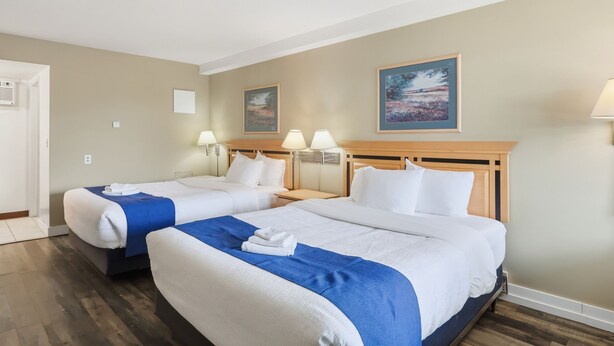 Ett hotellrum med två sängar, en sänggavel i trä, en tavla på väggen och en lampa på nattduksbordet.