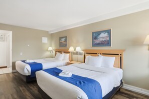 Habitación de hotel con dos camas, cabecera de madera, un cuadro en la pared y una lámpara en la mesita de noche.