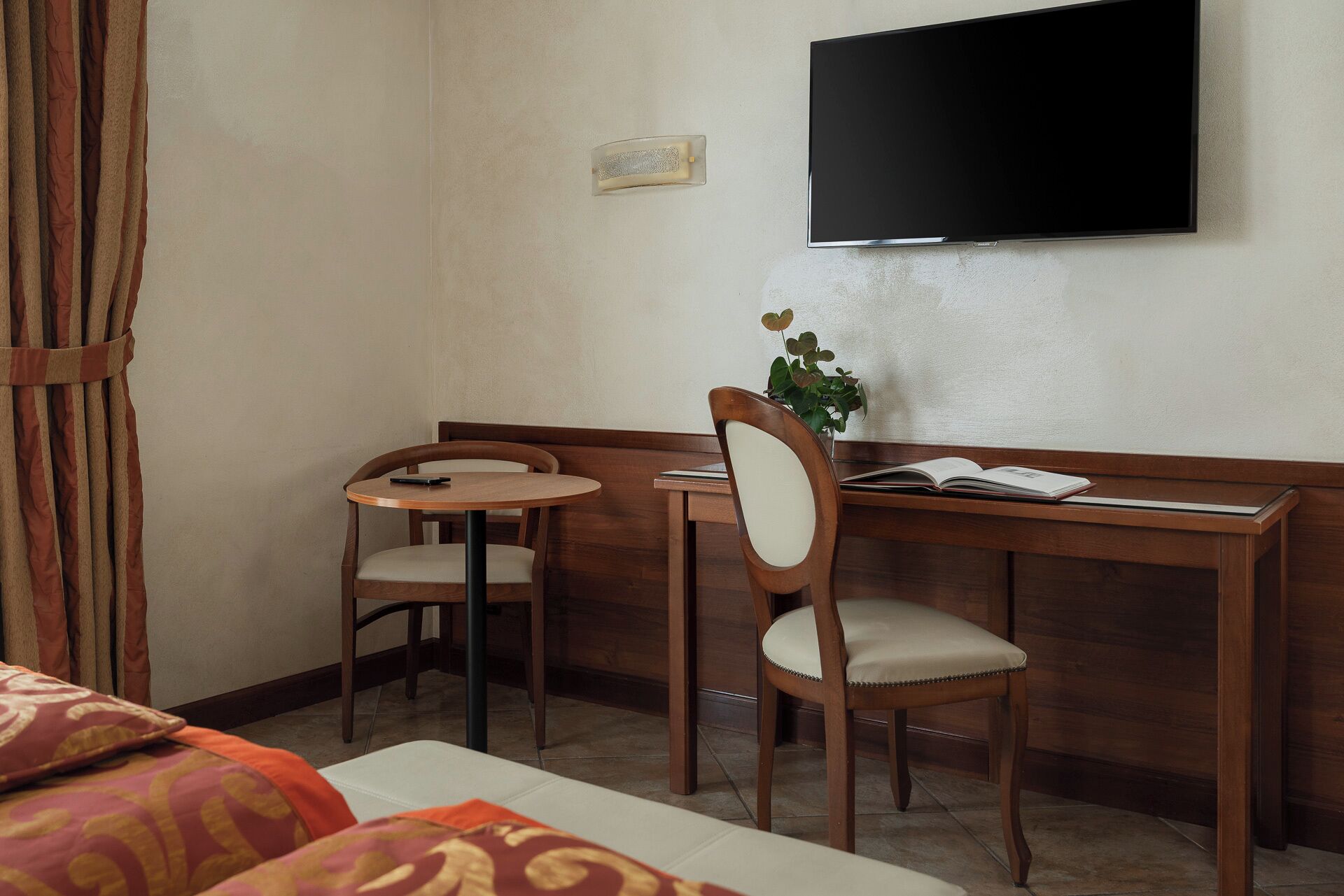 Ein Hotelzimmer mit Bett, Schreibtisch, zwei Stühlen, Fernseher und einer Pflanze.